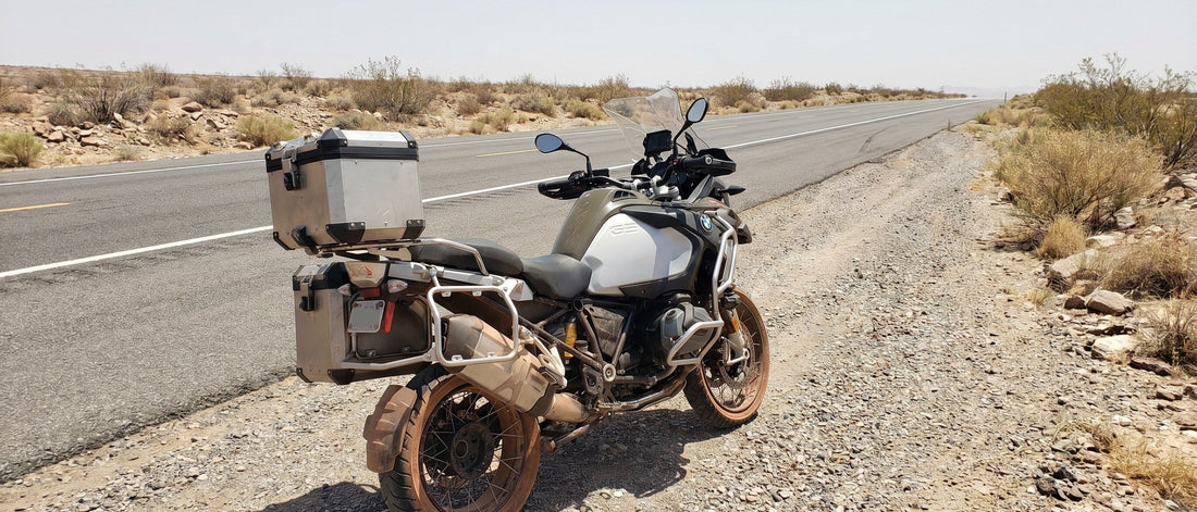 BMW R1250GS parked on desert highway shoulder in August heat, seat visible, empty road stretching into distance