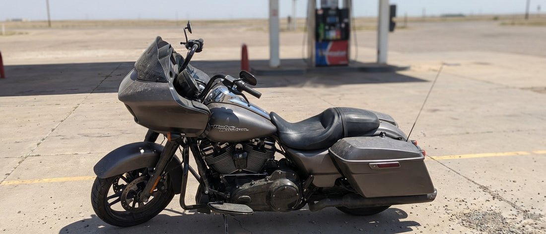 Harley Road Glide parked at a sun-baked gas station on a hot summer afternoon, heat shimmer on asphalt