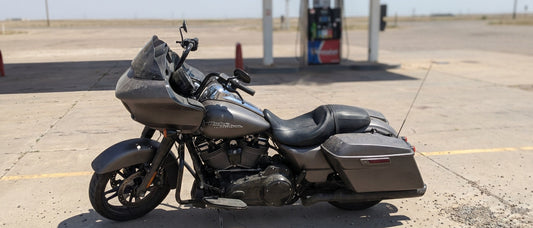 Harley Road Glide parked at a sun-baked gas station on a hot summer afternoon, heat shimmer on asphalt