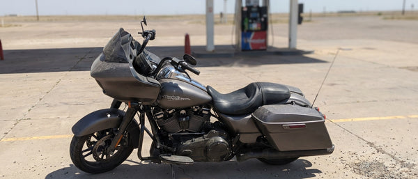 Harley Road Glide parked at a sun-baked gas station on a hot summer afternoon, heat shimmer on asphalt
