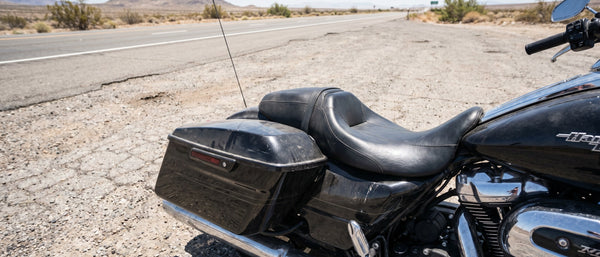 Harley Road Glide bagger parked at desert roadside pull-off, factory black vinyl seat baking in midday sun, long-ride fatigue